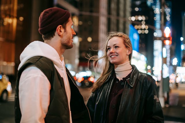 Man en vrouw kijken elkaar aan op straat, zij met een dromerige glimlach.