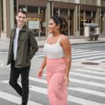 Jonge man en vrouw lopen lachend samen over een zebrapad, hij kijkt naar haar.