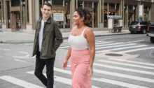 Jonge man en vrouw lopen lachend samen over een zebrapad, hij kijkt naar haar.