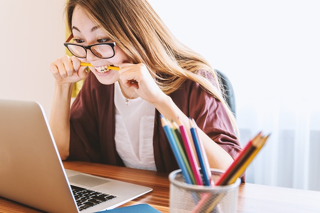 Vrouw achter laptop bijt gefrustreerd op potlood omdat haar ex haar jaloers heeft gemaakt.