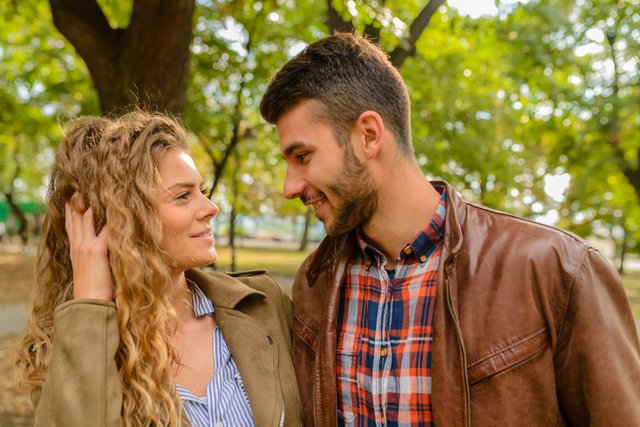 Man en vrouw die elkaar glimlachend in de ogen kijken, terwijl zij speels door haar haar gaat – symbool voor natuurlijk flirten en het herontwaken van aantrekkingskracht.