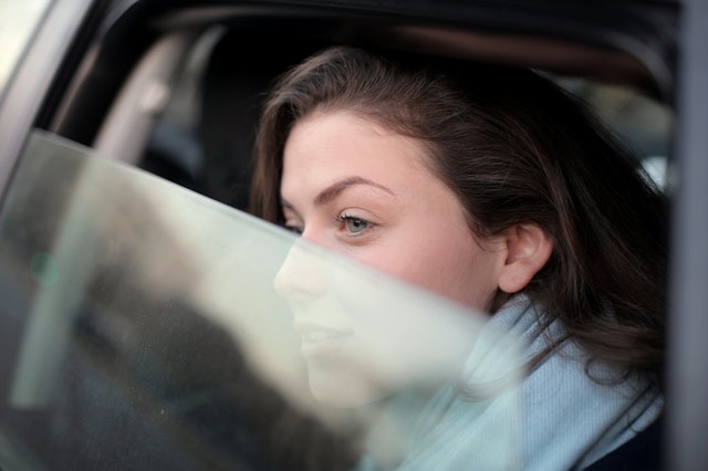 Jonge vrouw kijkt peinzend uit het zijraam van de auto.