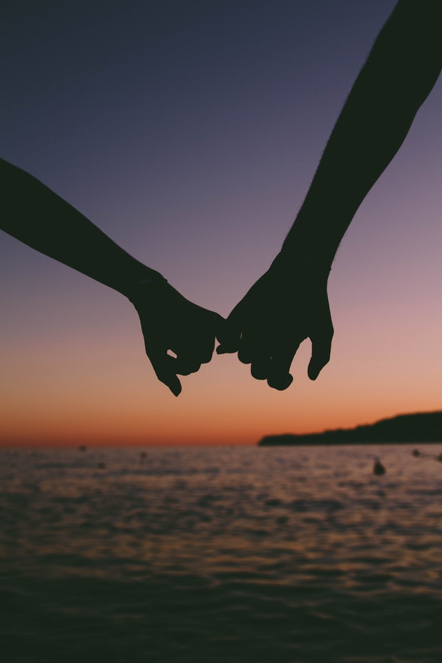 Silhouet van 2 handen die lkaar vasthouden bij het water na zonsondergang, als symbool voor het universum zijn ding te laten doen