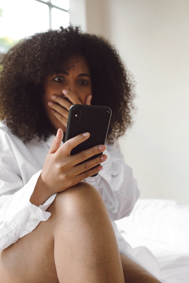 Vrouw kijkt verschrikt naar haar telefoon met een hand voor haar mond, dit is niet de reactie waar je op hoopt bij sexting met je ex.