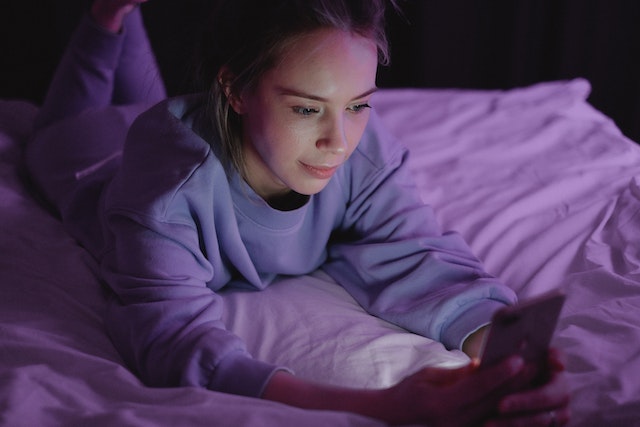 Vrouw ligt in bed met telefoon en laat zich meeslepen in sexting met haar ex.