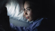 Vrouw ligt in het donker in bed en kijkt op haar telefoon, symbool voor sexting met je ex.