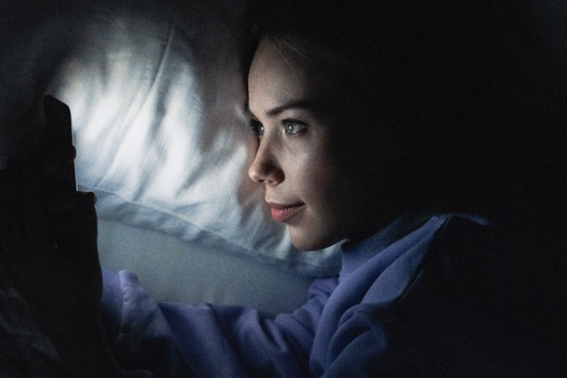 Vrouw ligt in het donker in bed en kijkt op haar telefoon, symbool voor sexting met je ex.