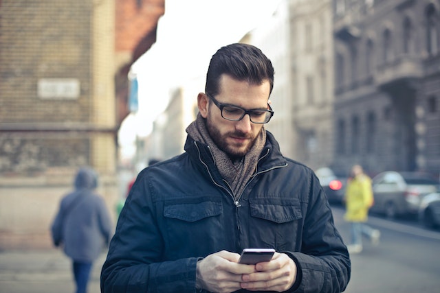 Man staat op straat en kijkt op zijn telefoon, het eerste voorzichtige contact na een relatiebreuk.