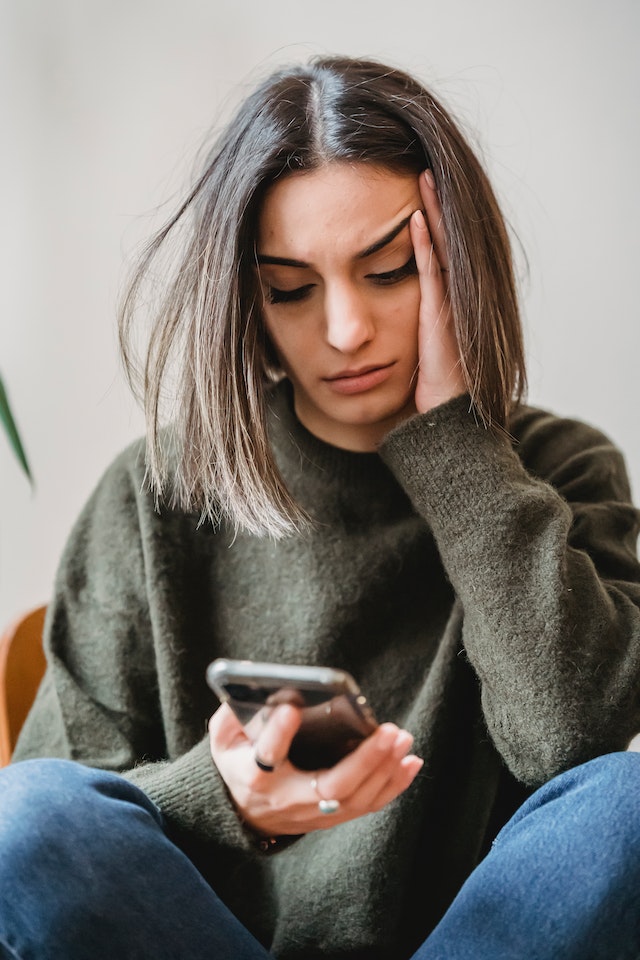 Vrouw leunt op haar hand en kijkt bezorgd naar haar telefoon.