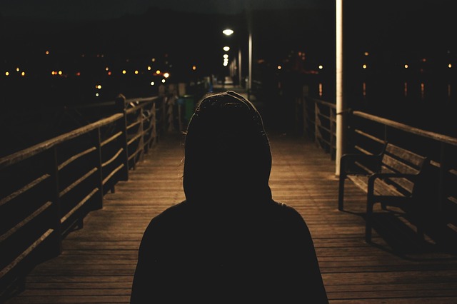Iemand met een donkere jas met capuchon op een slechtverlichte brug in het donker, symbool voor het stalken van je ex.