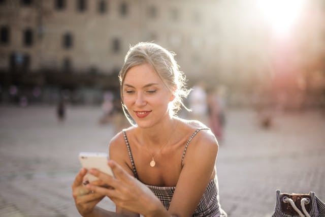 Jonge vrouw die glimlachend op haar telefoon kijkt, symbool voor het voorzichtig herstellen van contact met je ex.
