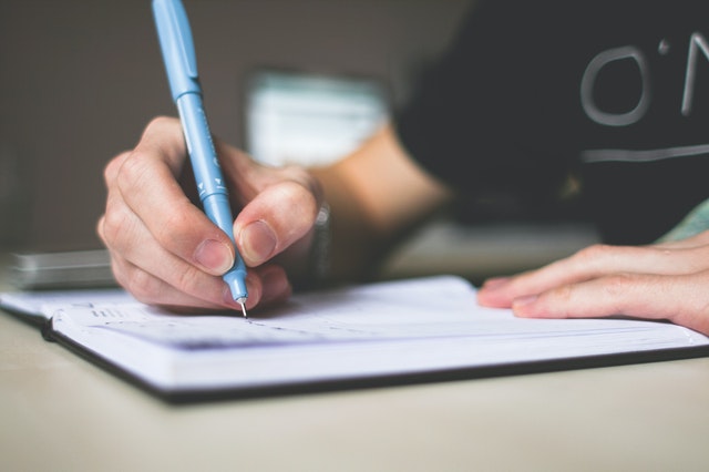 Hand met pen die schrijft in een notitieblok, symbool voor zelfreflectie na een relatiebreuk.