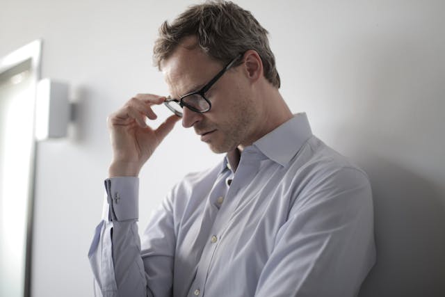 Man met licht voorover gebogen hoofd, houdt zijn bril vast en verlangt naar emotioneel begrip.