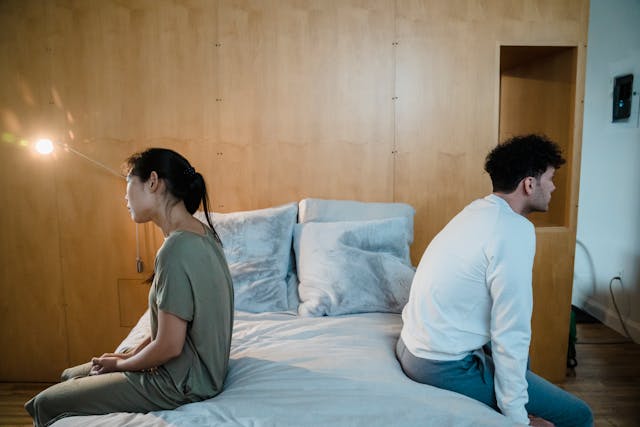 Man en vrouw zitten op de rand van het bed met de ruggen naar elkaar, zichtbaar vervreemd en zonder fysieke en emotionele intimiteit.