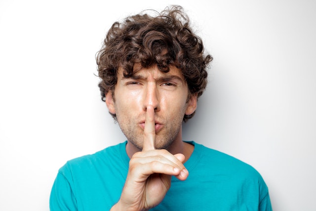 Man probeert zijn huwelijk te redden en maakt stiltegebaar om voorzichtigheid en geheimhouding te symboliseren.