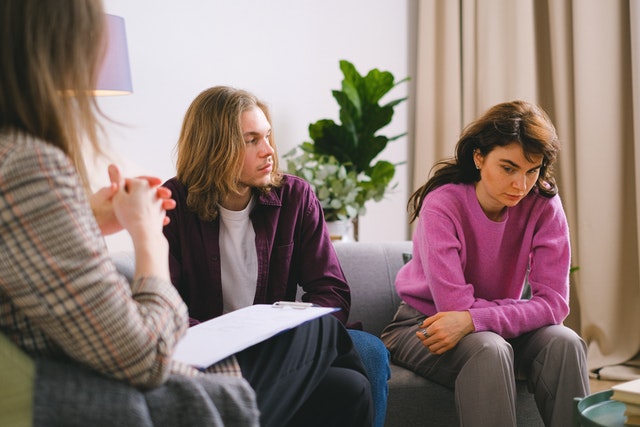 Een man kijkt zijn vrouw wanhopig aan tijdens huwelijkstherapie. Zij kijkt ongemakkelijk naar de grond en lijkt niet gemotiveerd om samen aan hun huwelijk te werken.