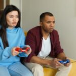 Man en vrouw zitten als vrienden naast elkaar op de bank te gamen.