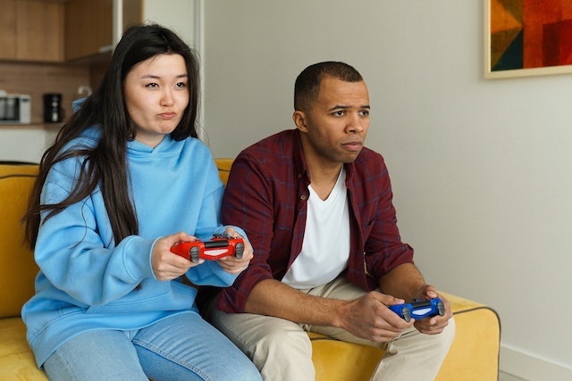 Man en vrouw zitten als vrienden naast elkaar op de bank te gamen.