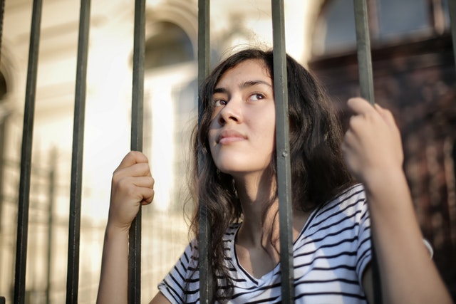 Vrouw met haar hoofd tussen de tralies, symbool voor gevangen voelen in een relatie.