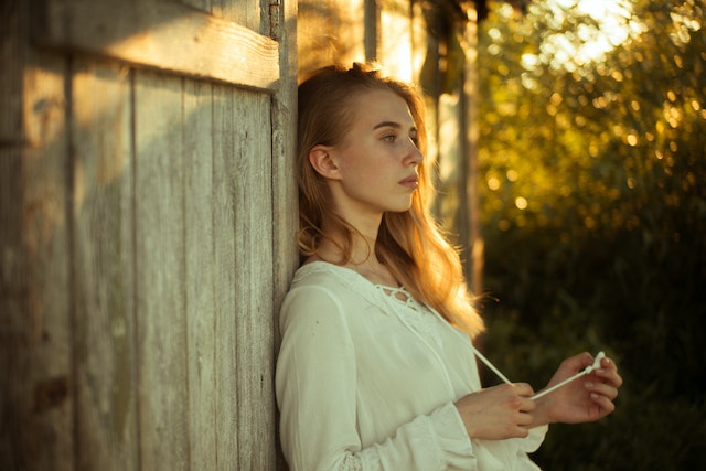 Vrouw leunt tegen een schutting aan en wacht af.