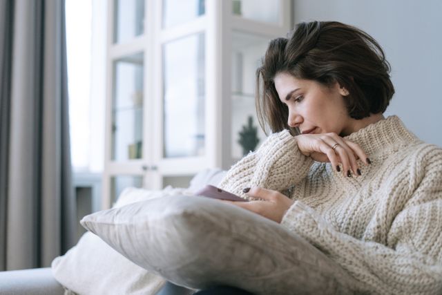 Vrouw kijkt verdrietig naar haar telefoon terwijl ze wacht op een reactie van haar ex.