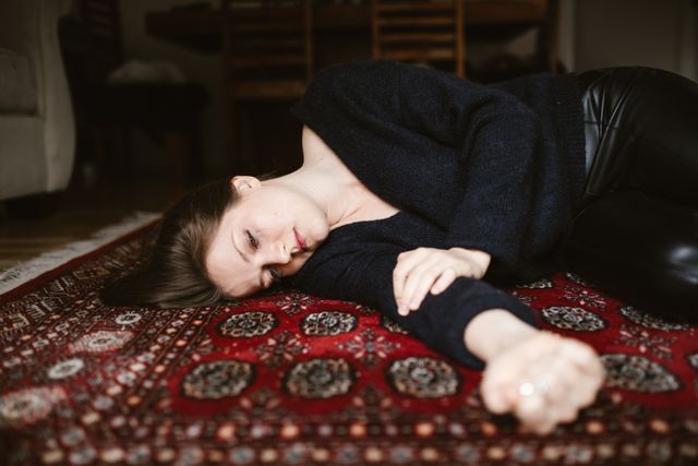 Vrouw ligt depressief op het tapijt op de grond, symbool voor de depressiefase na een gebroken hart.