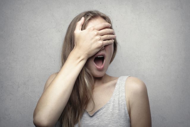 Vrouw houdt een hand voor haar ogen en roept nee, symbool voor de ontkenningsfase na een relatiebreuk.