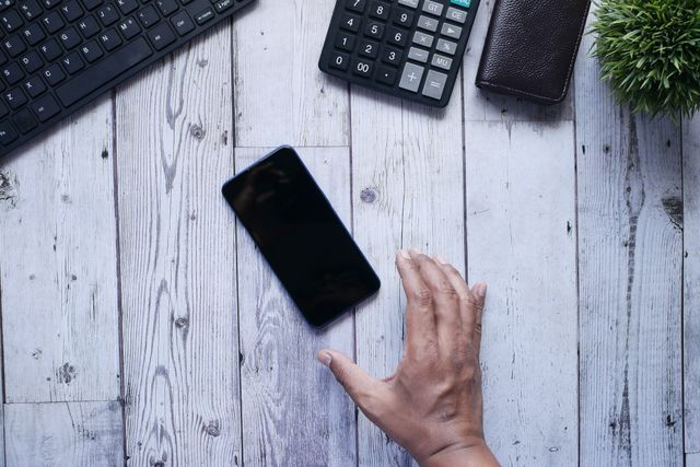 Hand reikt naar een telefoon op tafel, symbool voor de drang om contact te zoeken die je moet weerstaan na een gebroken hart.