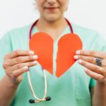 Persoon in medisch uniform houdt een doormidden gescheurd papieren hart vast, symbool voor het broken heart syndrome of gebroken hart syndroom.