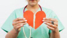 Persoon in medisch uniform houdt een doormidden gescheurd papieren hart vast, symbool voor het broken heart syndrome of gebroken hart syndroom.