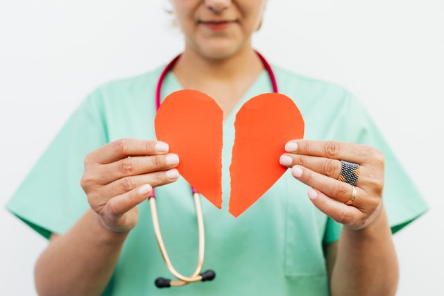 Persoon in medisch uniform houdt een doormidden gescheurd papieren hart vast, symbool voor het broken heart syndrome of gebroken hart syndroom.