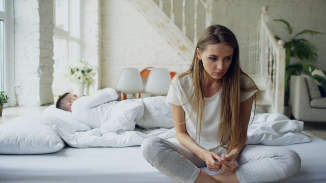 Hij ligt te slapen terwijl zij zich gebruikt voelt na seks met haar ex en starend op de rand van het bed zit.